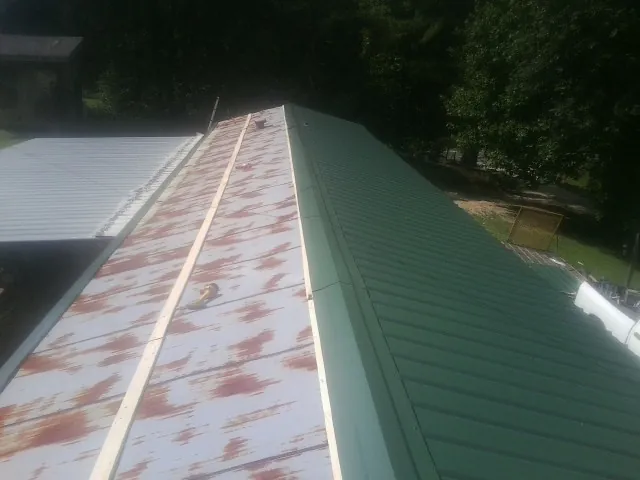 Old rusted panels beside newly installed green metal roofing — Wind Damage Roof Repair by Roofing Brothers in Sapelo Island