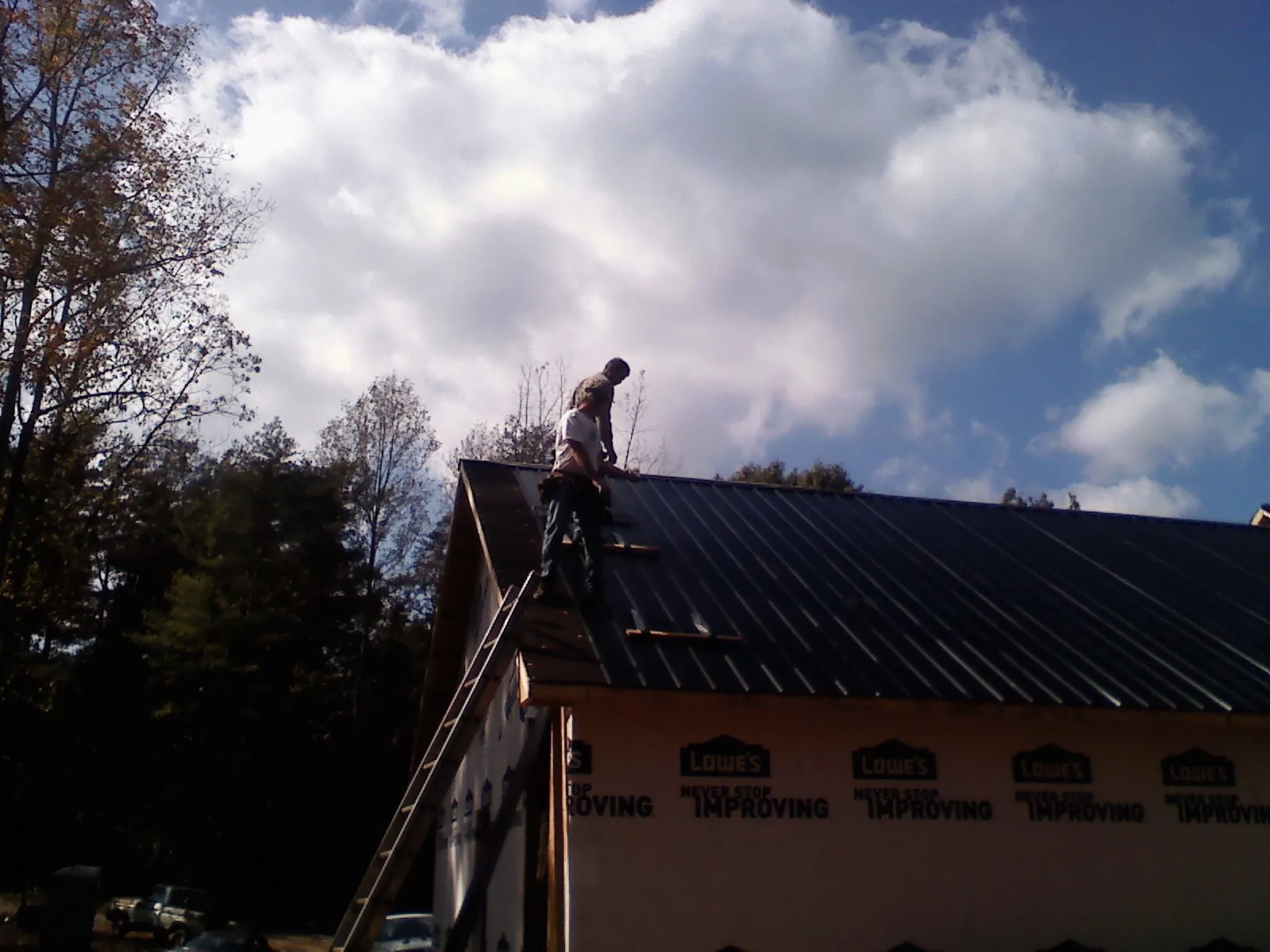 Roofer fastening dark metal panels high against a cloudy sky, from a Roof Inspection job in Sapelo Island