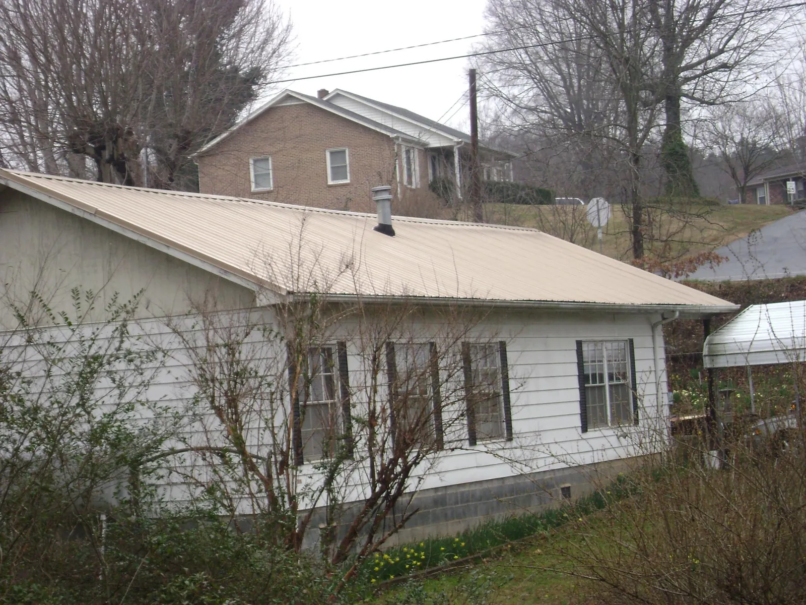 Tan metal roof on a white sided house set into a hillside — Commercial Roofing by Roofing Brothers in Sapelo Island